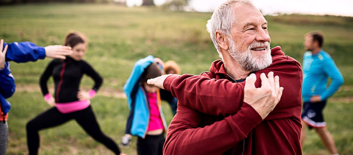 A large group of fit and active people doing exercise in nature, stretching.